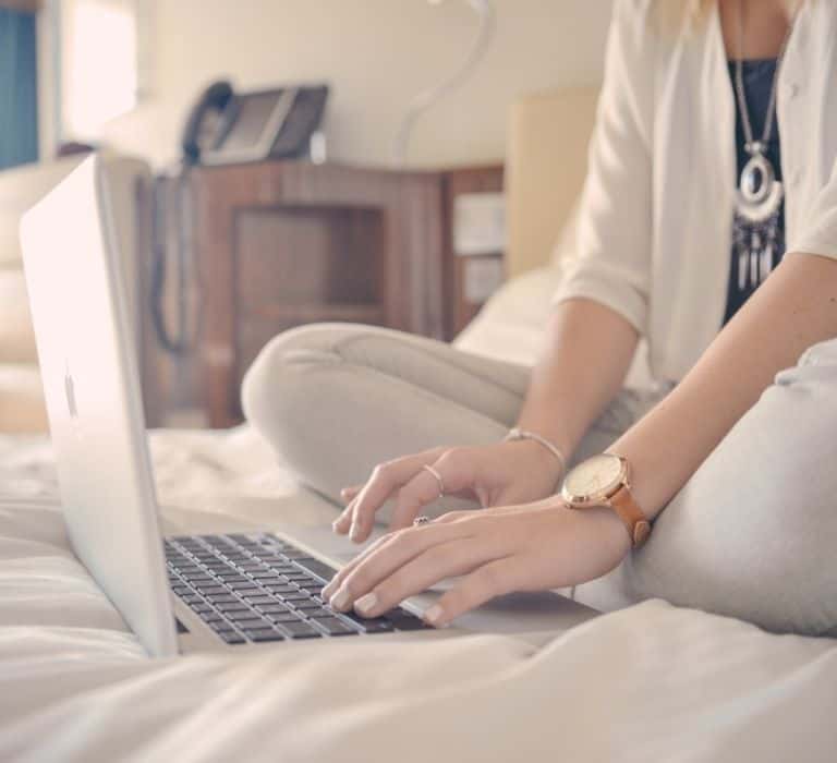a woman typing on a laptop on a bed
