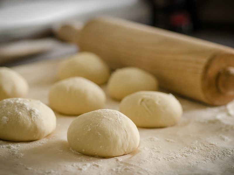 balls of dough sitting on a surface with a rolling pin in the background