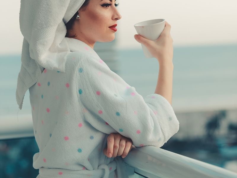 a woman sitting a cup of teak in a robe looking at the ocean