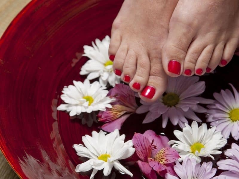 feet with red painted toe nails over a red bowl
