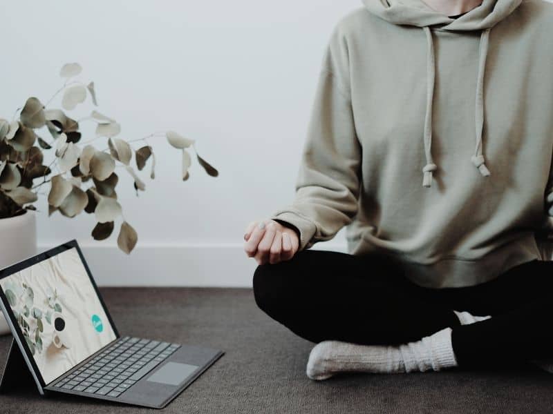 a person in sweats meditating on the floor next to a laptop