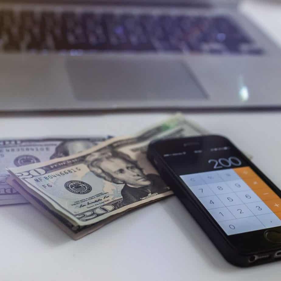 a phone caluclator and money on a table in front of a laptop