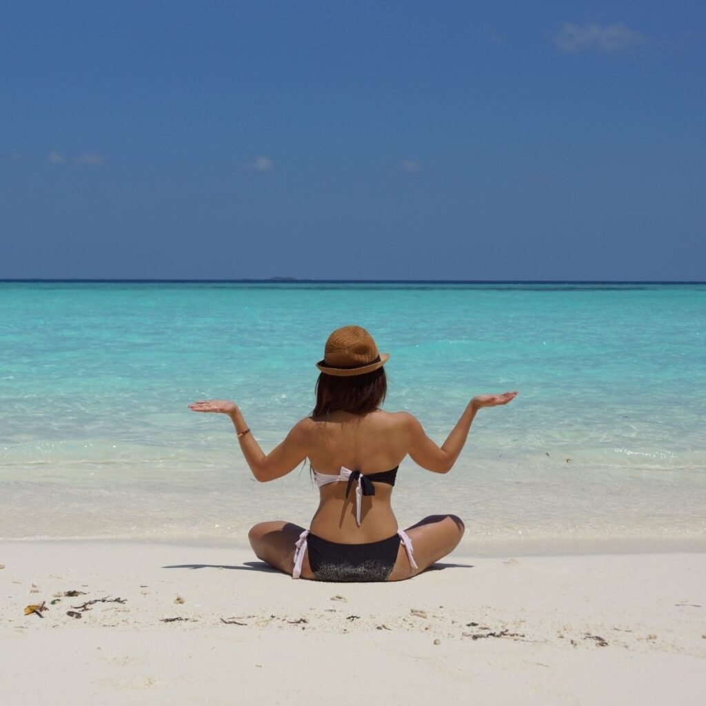 a girls sitting on a beach looking out at the water with her hands out