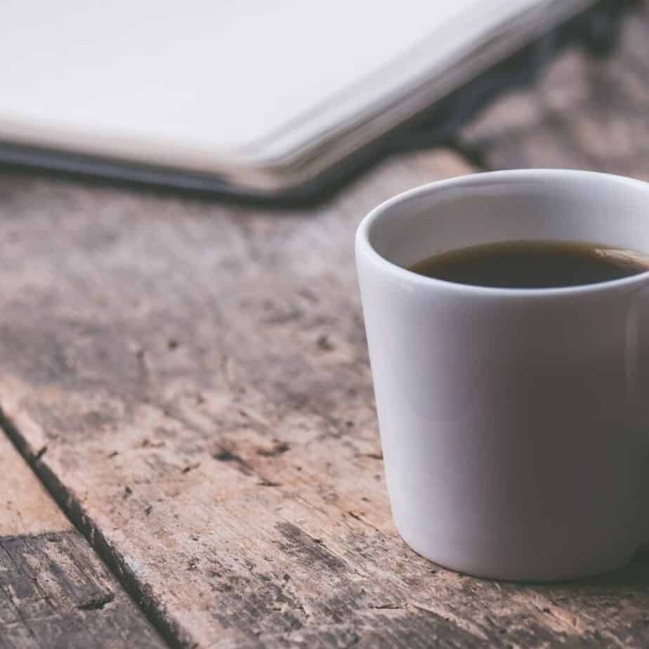 a cup of coffee on a wood table with notebook in the background