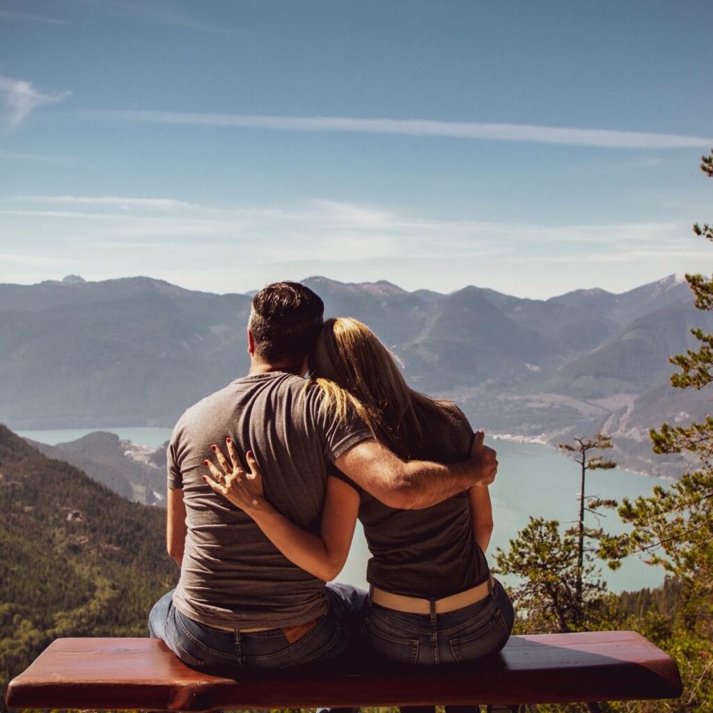 a couple sitting on a bench looking out at the mountains