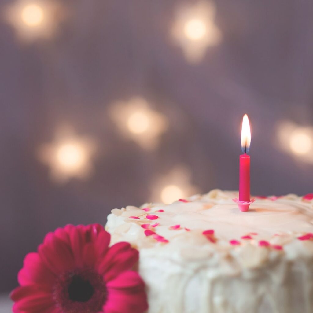 a birthday cake with a lit candle and pink flowers