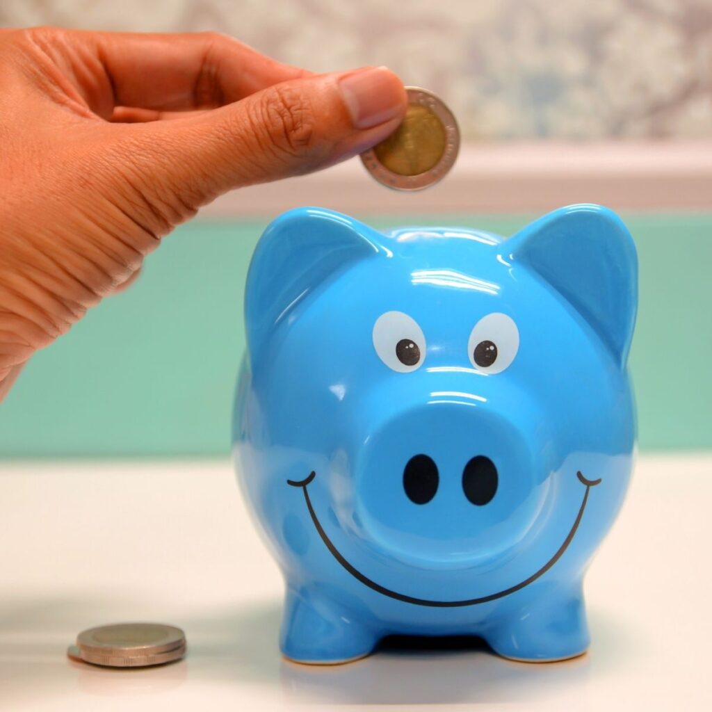 hands putting a coin in a blue piggy bank