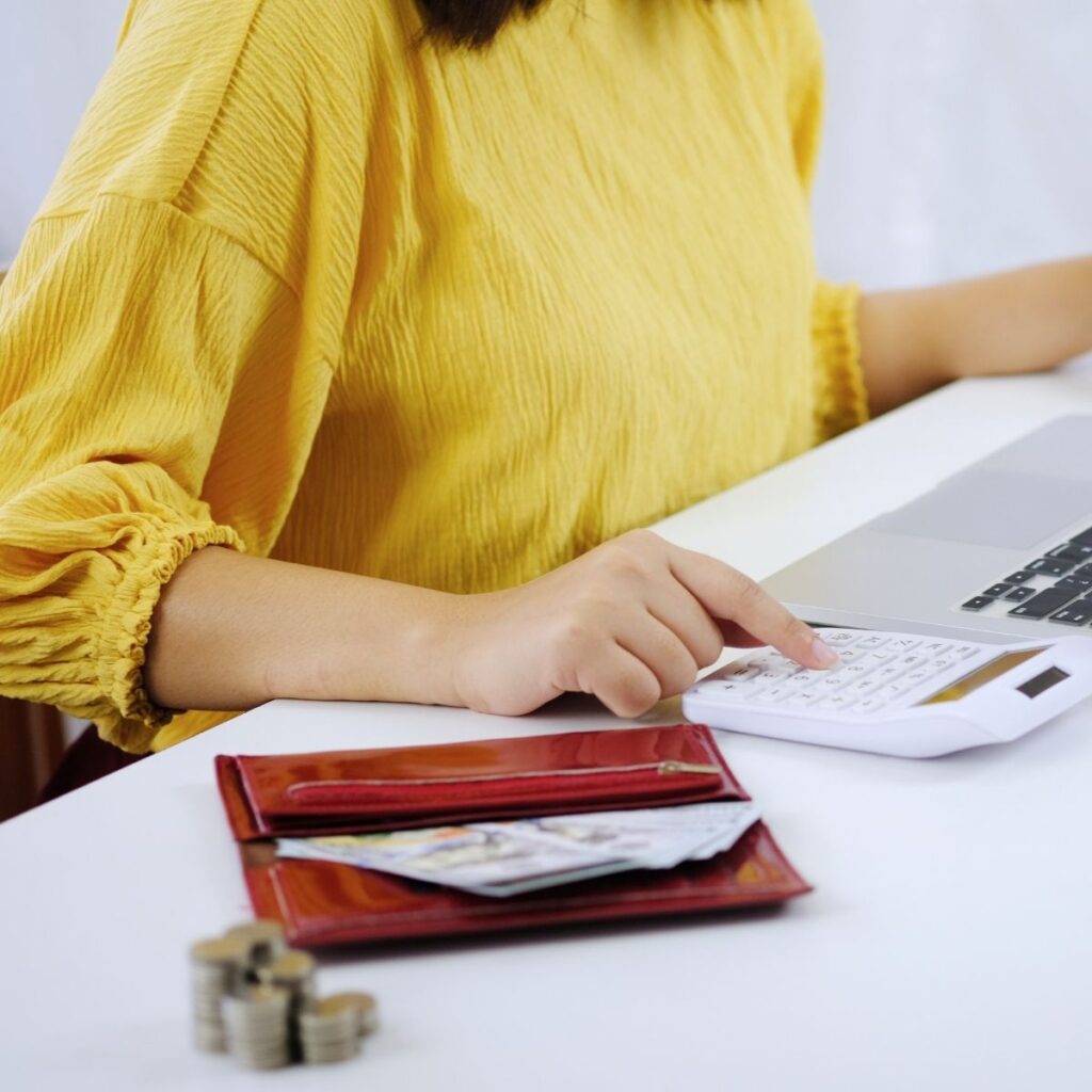 a woman using a calculator next to her laptop with an open wallet