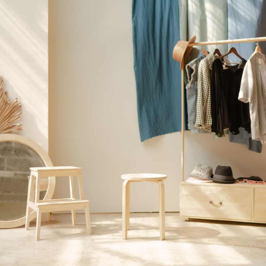 a closet with a wooden stool and clothes hanging
